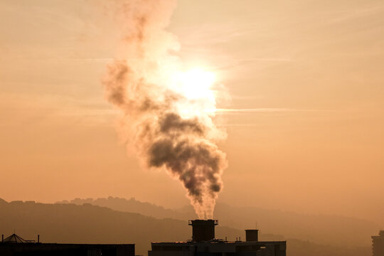 Aerial view of smoke billowing from an industrial chimney against a backdrop of hazy hills and a sun-drenched sky, Sarajevo, Federation of Bosnia and Herzegovina, Bosnia and Herzegovina.