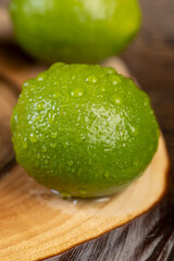 wet green ripe citrus scattered on the wooden table in the kitchen, ripe and juicy lime fruits for cooking, green limes covered with drops of water