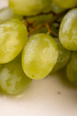 a branch of ripe beautiful green grapes on the table, covered with drops of water, wet fruits of pure green grapes on a branch on the table during cooking