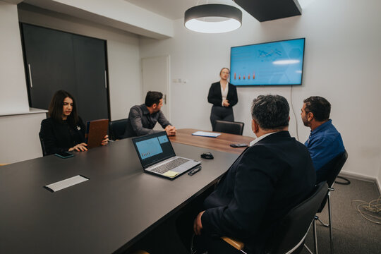 A group of business professionals in an office collaborating during a presentation with charts. - Powered by Adobe