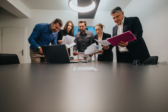 A team of professionals discussing documents and data around a laptop during a meeting.