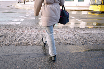 Woman in motion walking across messy slush patch at road crossing, winter street hazards, wet conditions, and the need for caution when navigating slippery pedestrian areas
