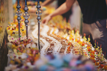 Guests enjoy a colorful dessert buffet featuring a variety of cakes and treats at a festive event in an elegant setting during the evening