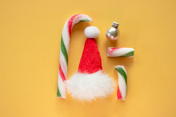 Christmas candies, elf hat and silver ornament on yellow background