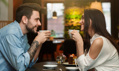 Young Lovers Enjoying Coffee Drinks Together During Romantic Date In Cafe. Love And Dating. Side View