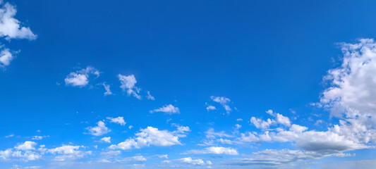 Clear blue sky panoramic background with small white clouds. The varying altitudes of the solitary clouds create a complex picture of the ease of flight and soaring above the earth.