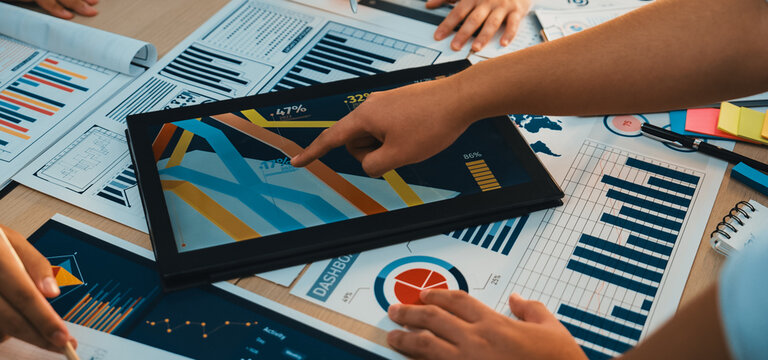A diverse team collaborates on business data analysis, reviewing charts and graphs on documents while brainstorming strategies to enhance performance in an office setting. SACTR
