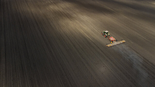 Aerial view of a lone tractor casts a long shadow as it tills the dark, fertile fields, creating stark lines in the soil, Osijek, Osijek-Baranja County, Croatia.