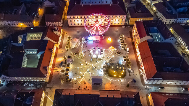 Aerial view of a brightly illuminated square featuring a Ferris wheel and festive lights nestled between buildings, creating a warm, inviting glow, Osijek, Osijek-Baranja County, Croatia.