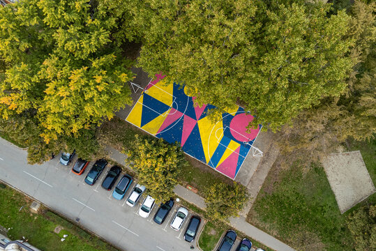 Aerial view of a vibrant basketball court, a geometric explosion of pink, blue, and yellow nestled amidst the green canopy of trees, Osijek, Osijek-Baranja County, Croatia.