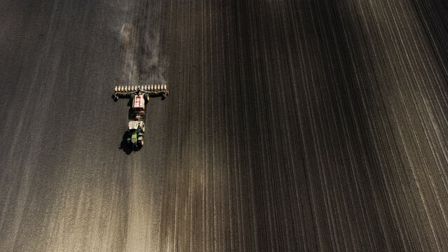 Aerial view of a tractor meticulously planting seeds, carving dark lines across the vast, earthy canvas, Osijek, Osijek-Baranja County, Croatia.
