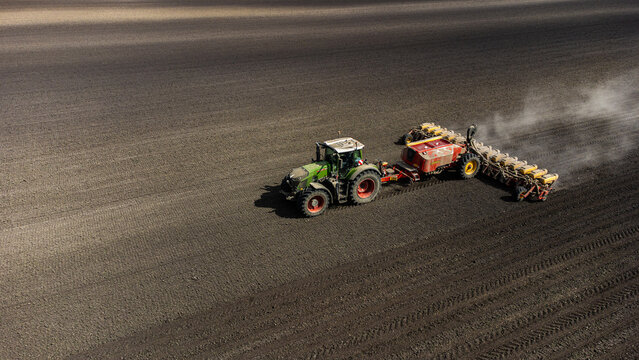 Aerial view of a tractor sowing seeds across the vast, dark field, dust billowing in its wake, contrasting against the light, open sky, Osijek, Osijek-Baranja County, Croatia.
