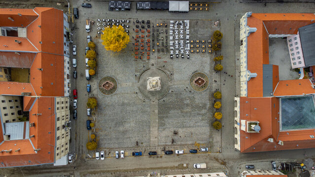 Aerial view of a structured square with a monument at its center, framed by buildings with red-tiled roofs, a golden tree, and rows of chairs, Osijek, Osijek-Baranja County, Croatia.