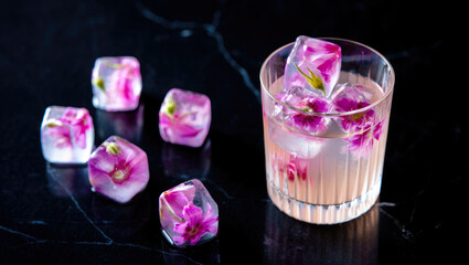 Floral ice cubes in cocktail glass on dark marble background, perfect for elegant beverage presentations and creative drink ideas. Trendy Refreshingly vibrant floral ice drink