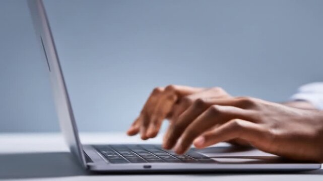 Close-up of hands typing on a laptop keyboard, blurred background, studio setting