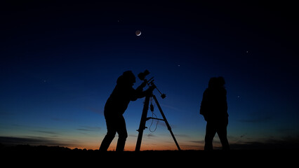 Fototapeta premium Amateur astro-photographers with a camera on a tripod photographing night sky with stars, planets, Moon and other celestial objects.