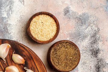 Sesame seeds and ground black pepper in small wooden bowls with raw garlic cloves
