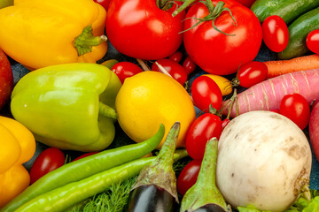 Colorful arrangement of fresh vegetables including bell peppers, tomatoes, lemon, and eggplant