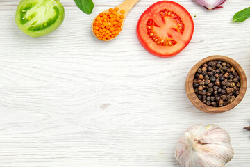 Spices and vegetables border including black pepper, lentils, tomato and garlic on white wood