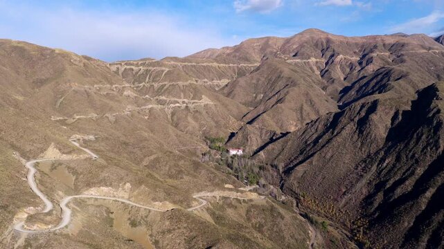 Slow panoramic drone movement reveals winding Caracoles de Villavicencio road tracing arid Andean slopes, gradually exposing Gran Hotel Villavicencio surrounded by sparse forest, Mendoza, Argentina