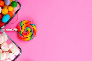 Vibrant rainbow lollipop with gum and marshmallows on a bright pink background