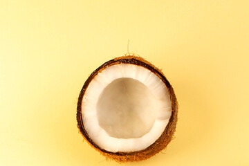 Fresh half coconut cut open revealing white flesh on a bright yellow background