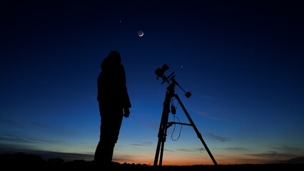Fototapeta premium Amateur astro-photographer with a camera on a tripod photographing night sky with stars, planets, Moon and other celestial objects.