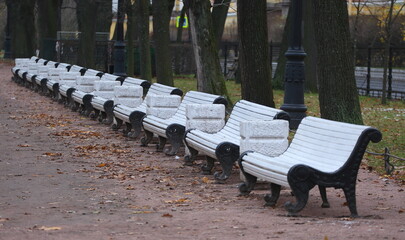 A row of white wooden benches in an autumn public park, Alexander Garden, Saint Petersburg, Russia, November 17, 2025