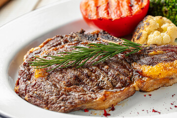 Juicy grilled steak served with roasted tomato cauliflower and fresh rosemary garnish on plate