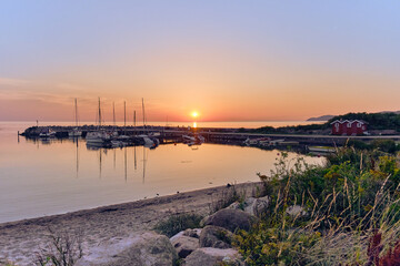 Fototapeta premium A peaceful sunset scene overlooking Lerhamn harbor and Kattegat, with warm light reflecting on water and several swimmers standing in silhouette on pier, capturing a tranquil coastal moment in Sweden