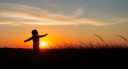 Silhouette of a young child with arms outstretched at sunset.