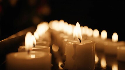 Row of burning white candle light in dark room. Warm memorial illumination for funeral, vigil, or prayer service.