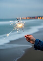 Sparkler held by a hand on the beach at dusk with ocean waves in the background