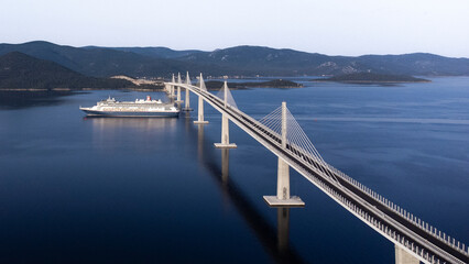 Komarna, Croatia - 14 November 2025: Aerial view of the majestic Peljesac Bridge piercing through the calm, deep blue Adriatic Sea, a cruise ship gracefully sailing beneath its elegant arches.