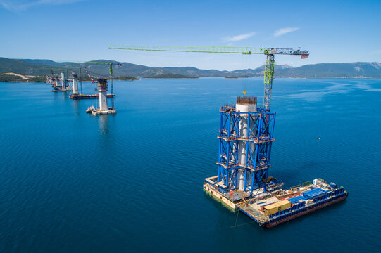 Komarna, Croatia - 14 November 2025: Aerial view of the Peljesac Bridge construction with its towering pillars rising from the shimmering Adriatic Sea under a clear azure sky.