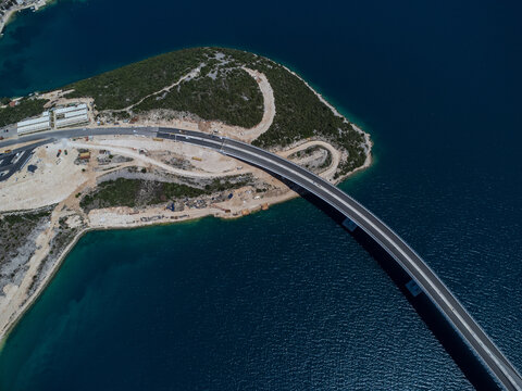 Aerial view of the striking bridge curving across the turquoise waters near a rugged coastline, Komarna, Dubrovnik-Neretva County, Croatia.