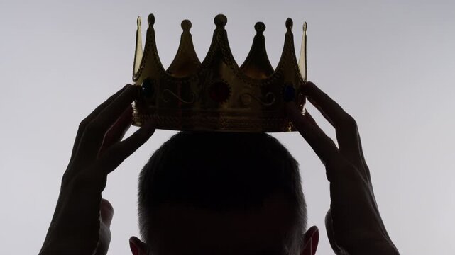 A silhouette of a man placing a crown on his head. Concept of greatness and leadership.