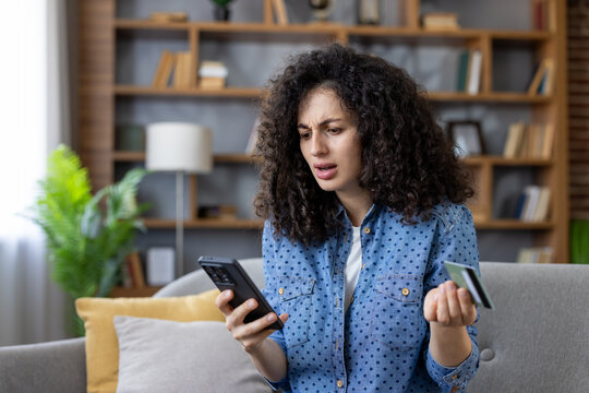 Woman feeling frustrated and confused while trying to make an online payment with a credit card and smartphone, indicating a problem or declined transaction