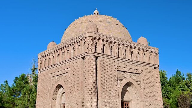 A clear daytime view of the exterior of the Ismail Samani Mausoleum in Bukhara, Uzbekistan, showing baked-brick patterns and rounded architectural features.