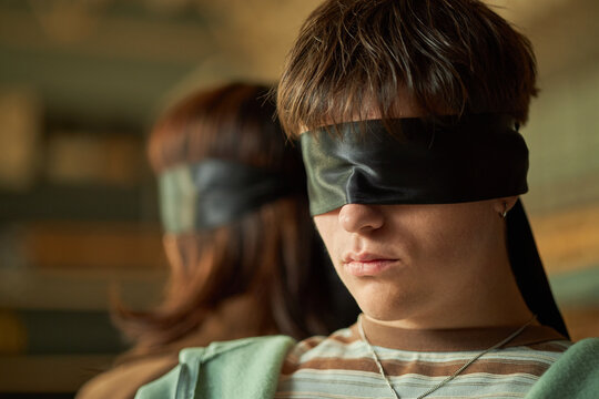 Caucasian teenage boy and teenage girl sitting back to back wearing black blindfolds participating in psychology experiment focused on sensory perception and student behavior