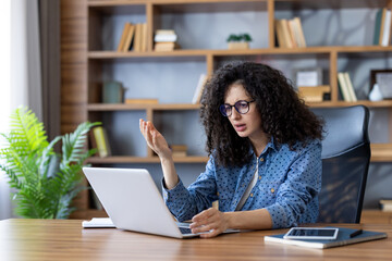 Young woman sitting at a desk, looking frustrated and confused at her laptop screen, encountering a technical problem or system error during a remote work session at her home office