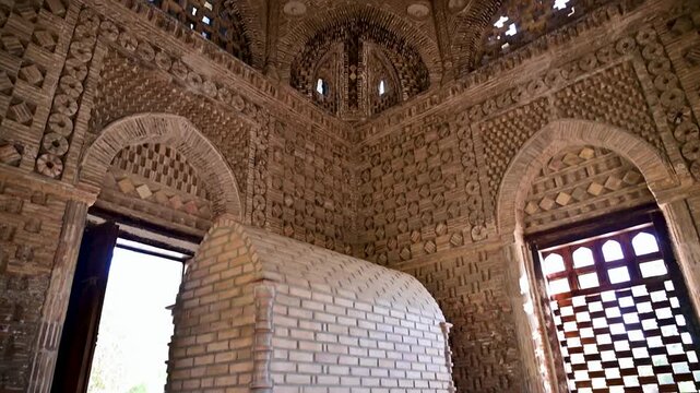 An interior view of the Ismail Samani Mausoleum in Bukhara, Uzbekistan, featuring patterned brickwork, arches, and warm natural light inside the historic tomb.