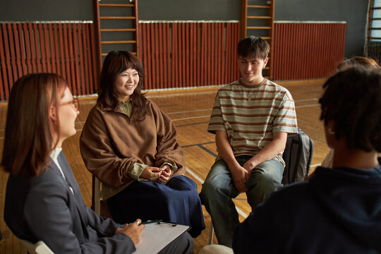 Group of multiethnic teenagers and young adult woman sitting in circle discussing psychology topics, smiling and engaging in conversation during group session