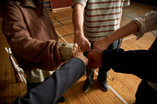 Group of multiethnic teenagers joining fists in unity, gymnasium floor background, demonstrating teamwork and collaboration during psychology class activity for students