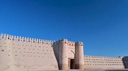 A clear daytime view of the old city wall and entrance gate of Bukhara, Uzbekistan, built from traditional mud-brick materials. The scene highlights the defensive architecture and historic setting of 