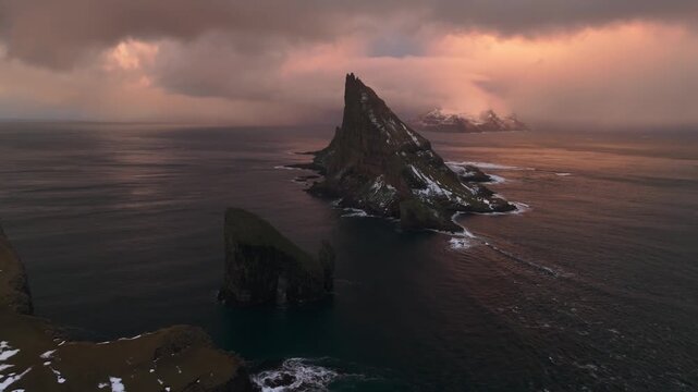 Aerial view of the dramatic Drangarnir sea stack and Tindholmur islet rising from the dark ocean under a moody sky, Streymoy, Faroe Islands.