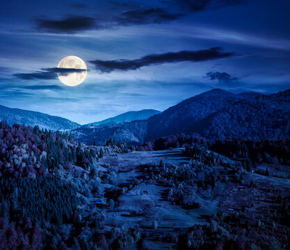 rural area in mountains autumn landscape at night. beautiful countryside scenery with rolling hills under dark sky in full moon light. backdrop for fiction art or mystery concepts