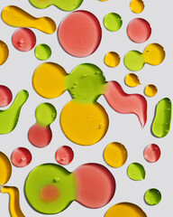 Swatches of shower gel drops of different shapes in yellow, green and red on a white background