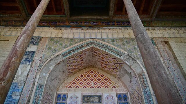 A detailed view of the Bolo Hauz Mosque facade in Bukhara, Uzbekistan, showing carved wooden columns, decorative patterns, and traditional Islamic architectural elements.
