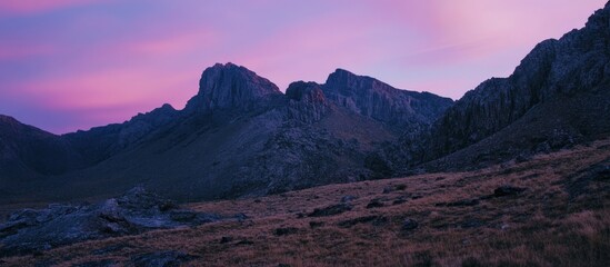 Dramatic mountain landscape at dusk with a vibrant pink sky highlighting the rugged peaks